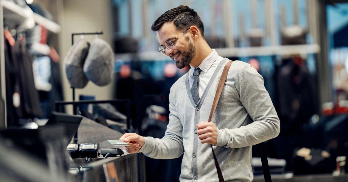 Man stands at a checkout counter about to pay for a purchase in a clothing store using a loyalty rewards card.