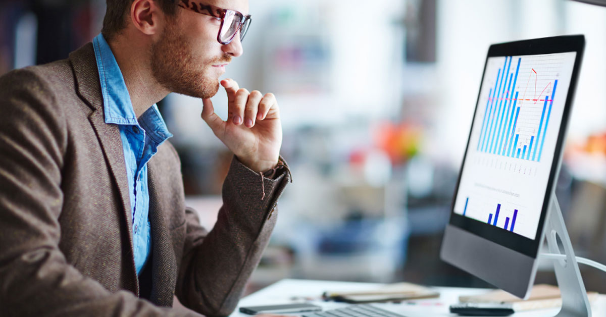 Man sits at a computer desk checking the unified monitoring performance dashboard on a computer screen.