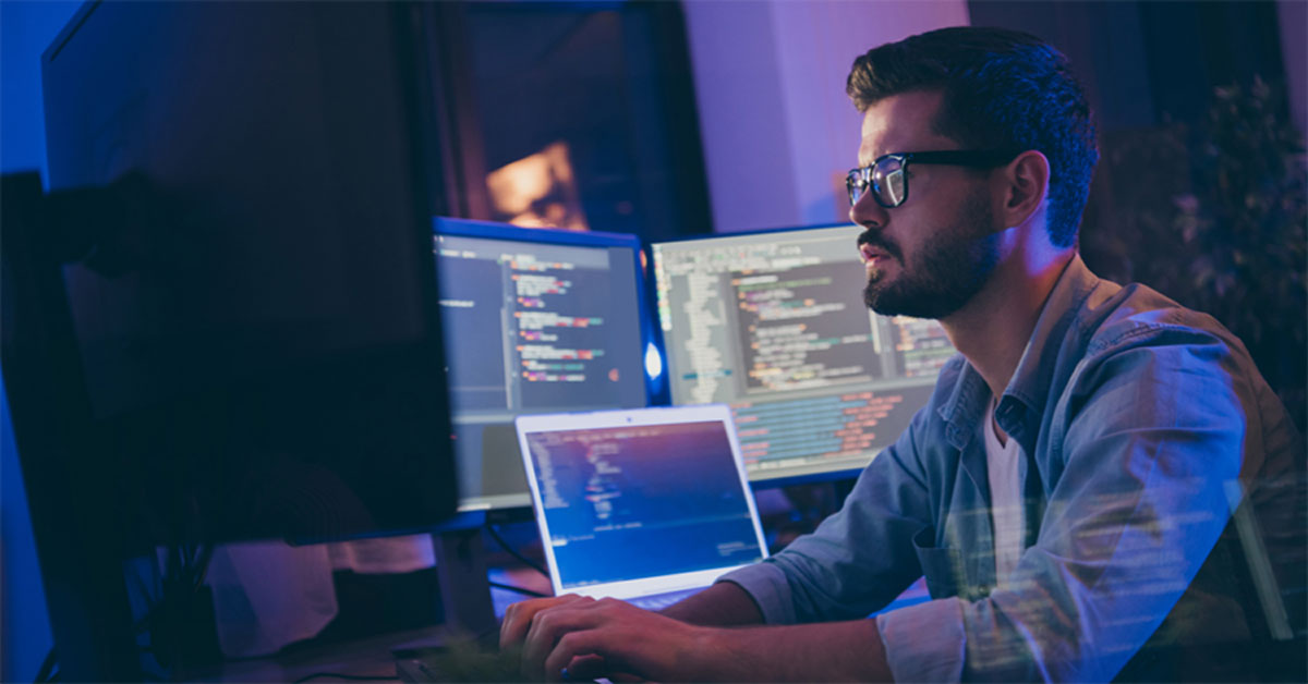 man-typing-coding-language-onto-a-triple-monitor-computer-screen
