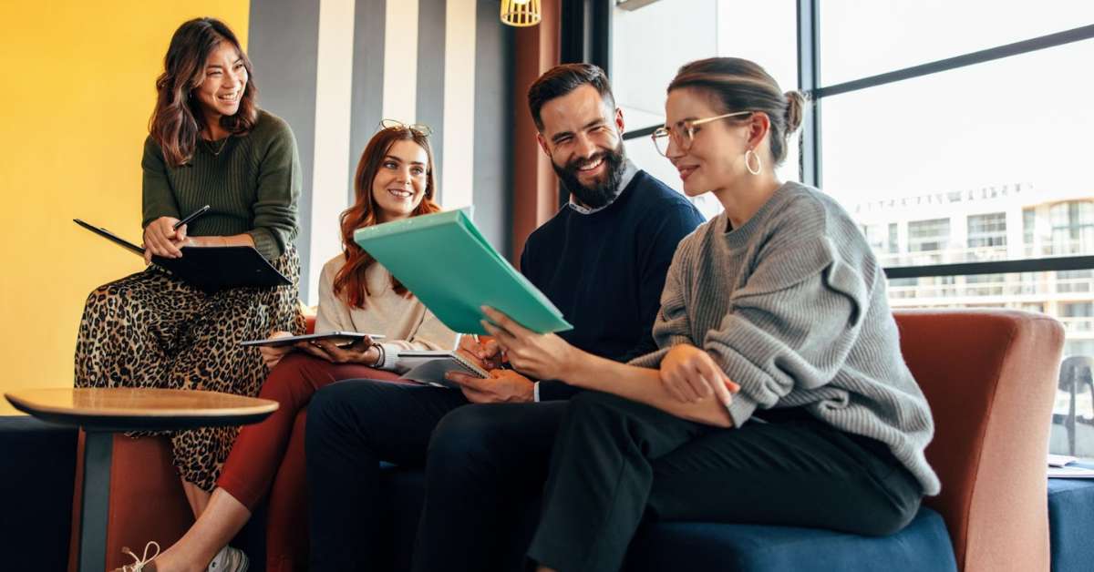 A group of colleagues casually sit together at a table laughing while working.