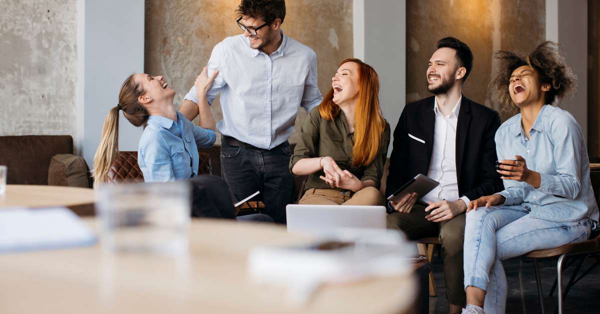 a group of coworkers sit around a conference table and laugh showing how Agile methodology can be fun.